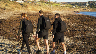 Three people walking with weighted backpacks on a beach