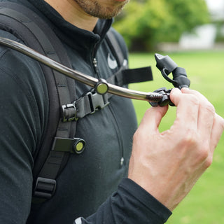 Person adjusting a backpack strap with a blurred green outdoor background